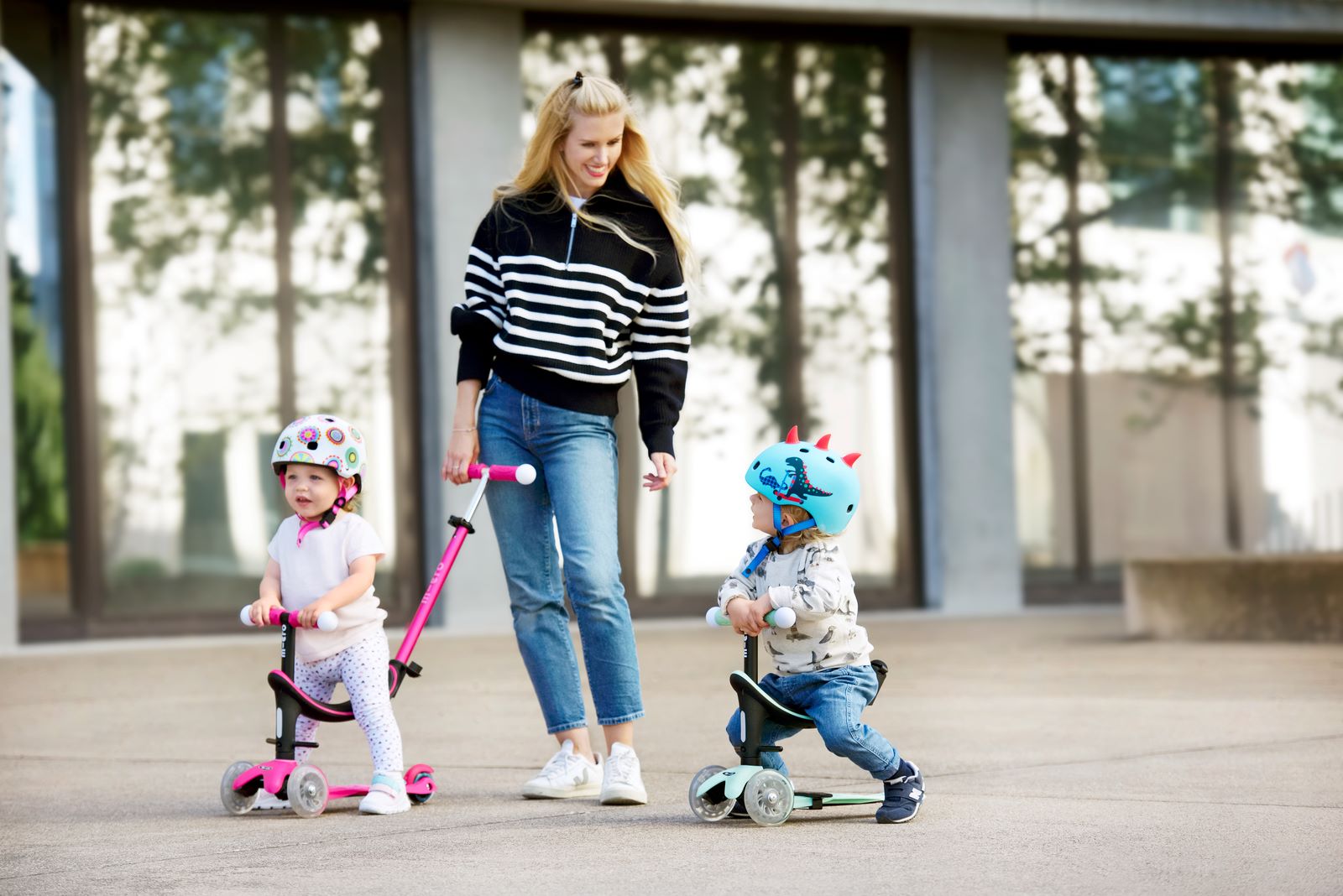 deux petits enfants sur leur trottinette avec siège bébé roulant avec leur maman 