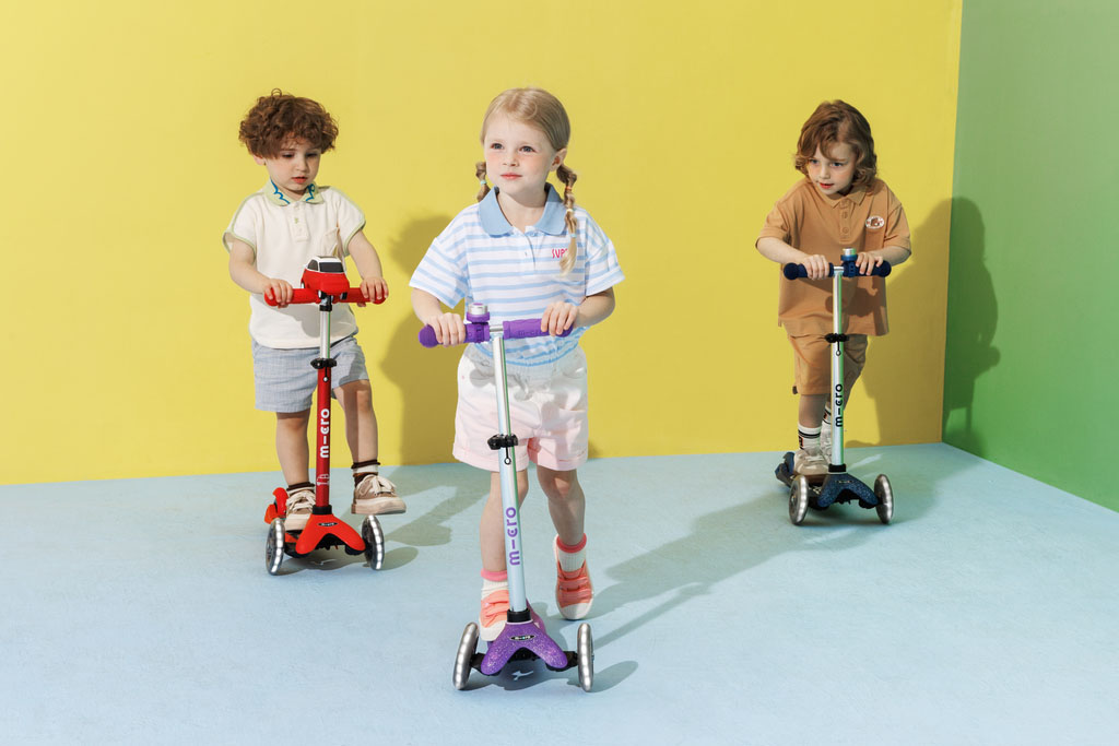 trois enfants de différents âges en train de faire de la trottinette