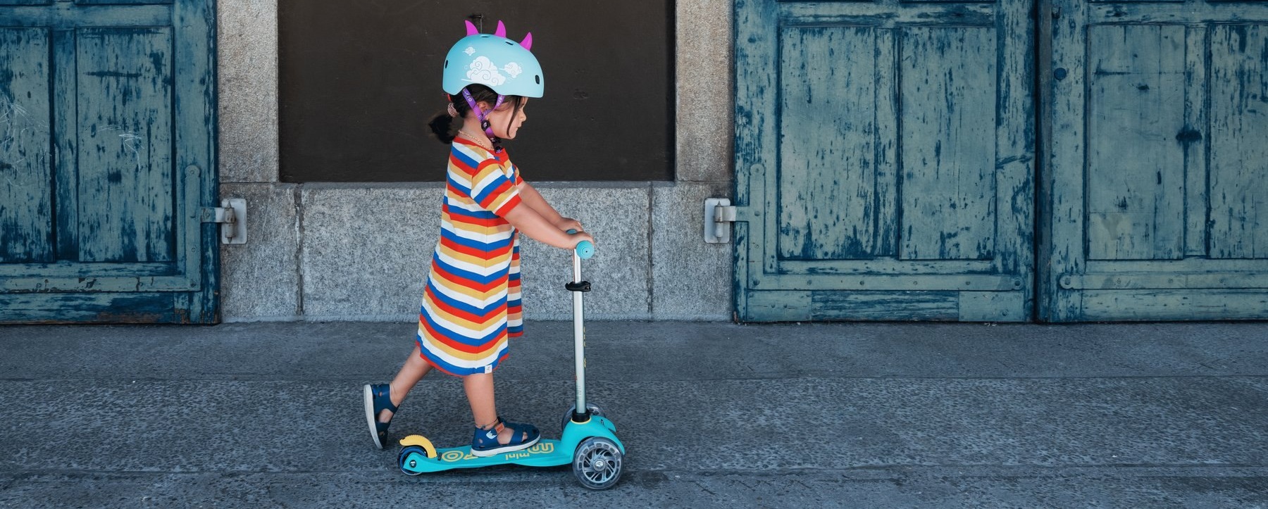 Enfant en trottinette Micro devant une porte en bois patinée