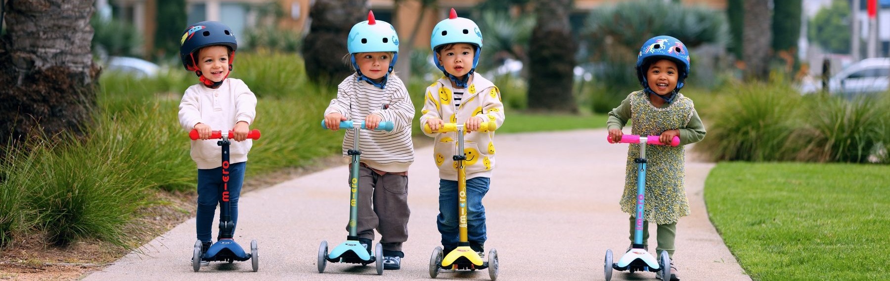 Quatre enfants portant un casque roulent en trottinette Micro dans un parc