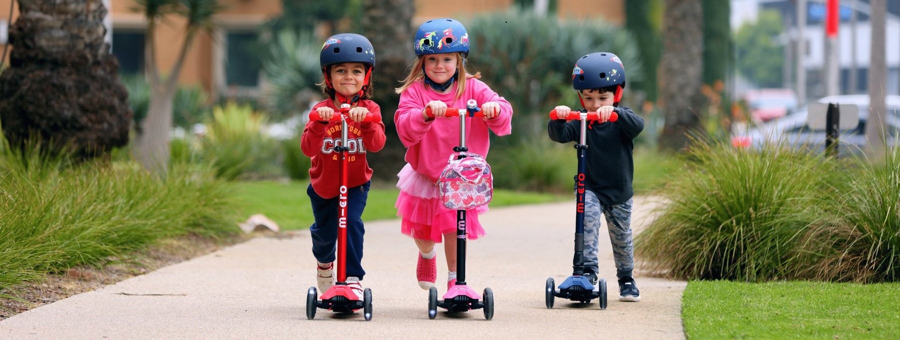 Trois enfants en trottinette Micro dans un parc